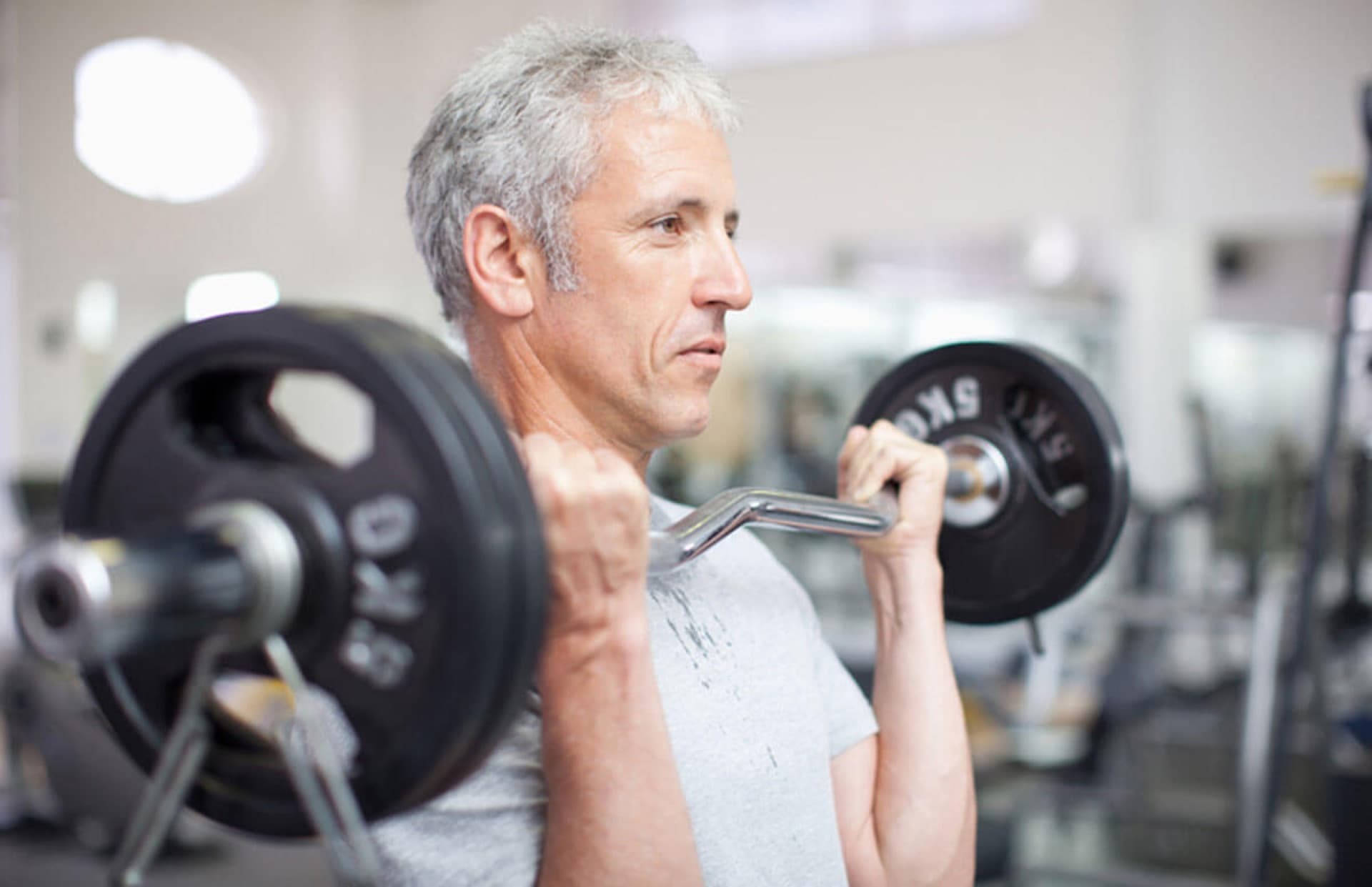 Silver-haired mature male doing barbell curls — a man over 40 keeping strength signals working