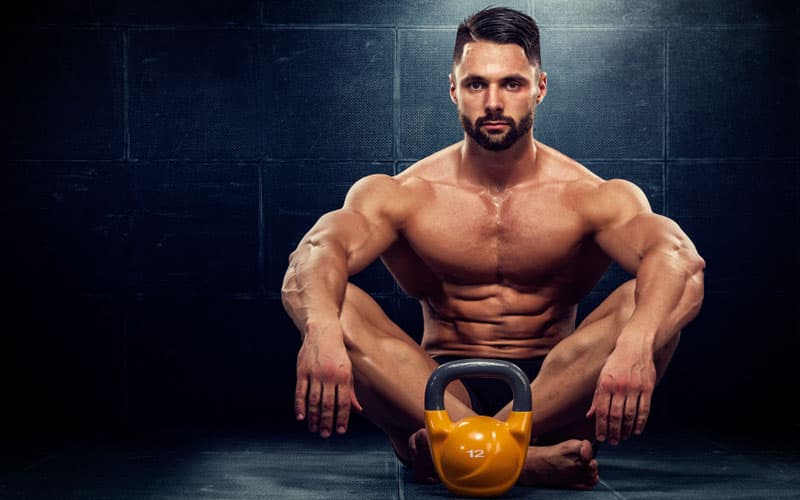 Athletic man with a kettlebell in a dark gym — strength and energy that come from properly managed testosterone